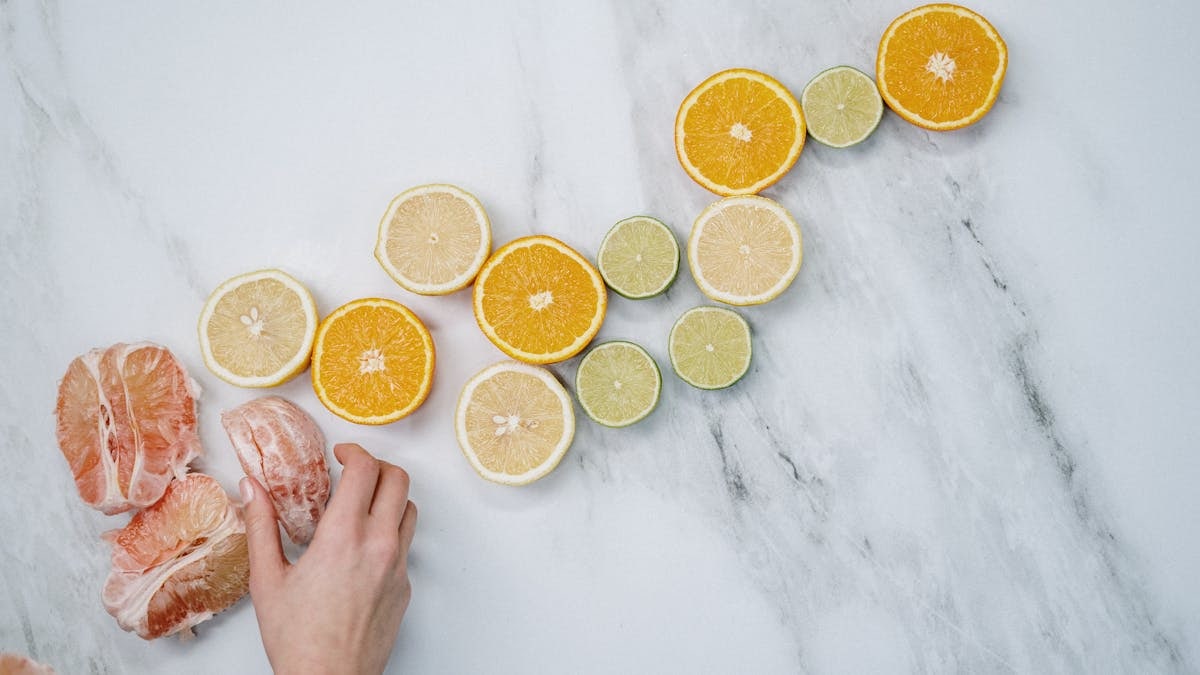 Overhead view of assorted citrus slices and a hand on a marble surface. Fresh and vibrant composition.